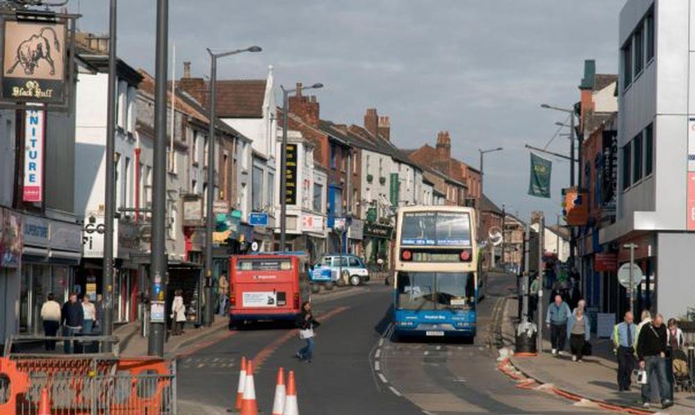 Double decker buses on busy UK high street with shops - Manchester Airport Taxi Transfer - Manchester Airport Taxi Transfer