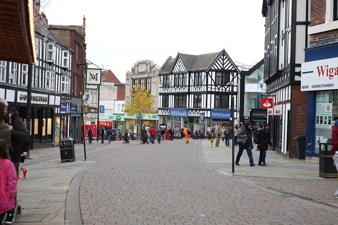 Wigan high street with Tudor buildings, WHSmith, and shoppers. - Manchester Airport Taxi Transfer - Manchester Airport Taxi Transfer