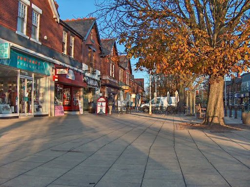 Quiet UK high street with autumn trees and brick shops. - Manchester Airport Taxi Transfer - Manchester Airport Taxi Transfer