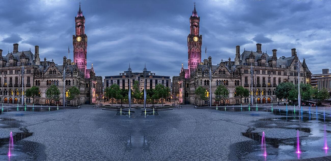Symmetrical view of Manchester Town Hall at dusk with colorful fountain lights in the foreground. - Manchester Airport Taxi Transfer - Manchester Airport Taxi Transfer