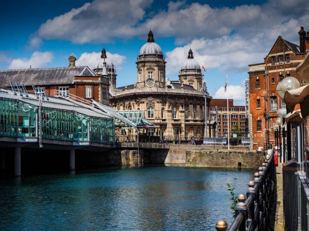 Grand neoclassical building with domed towers along a canal, connected by a glass pedestrian bridge under a blue sky. - Manchester Airport Taxi Transfer - Manchester Airport Taxi Transfer