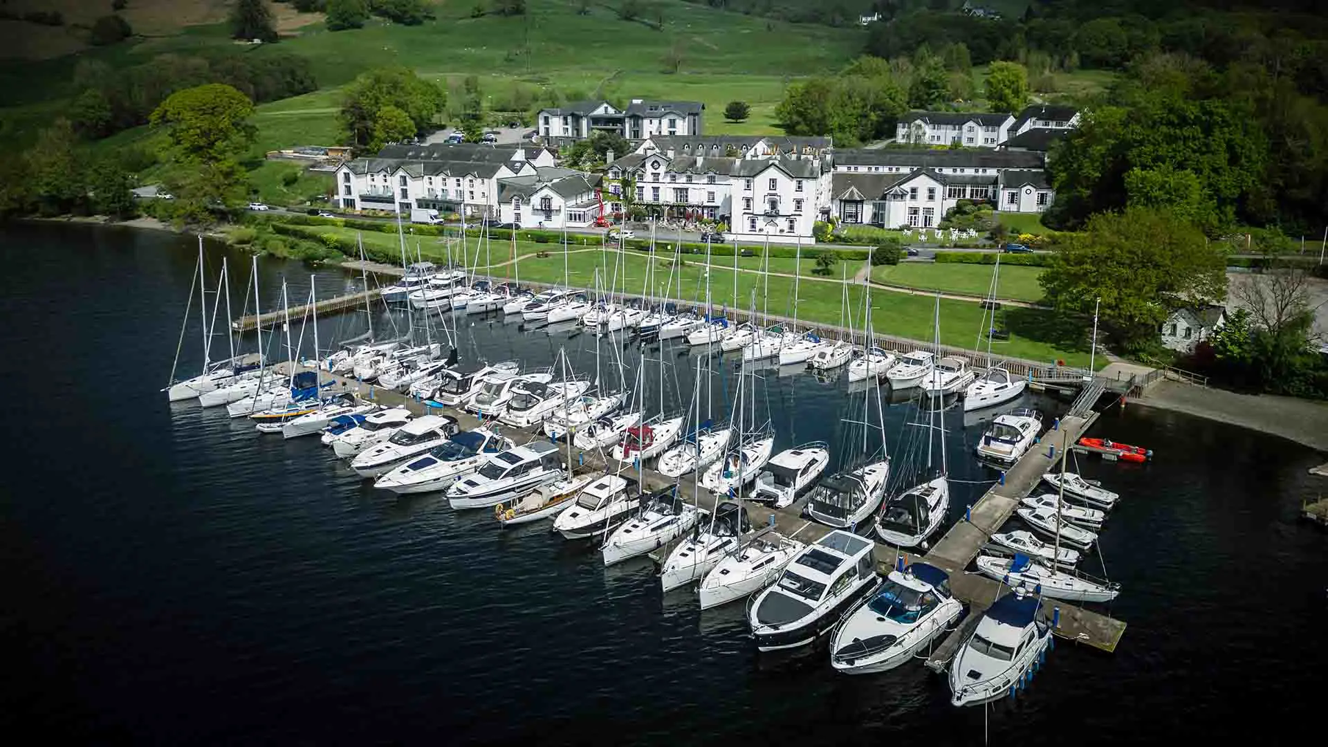 Marina with numerous sailboats and yachts docked along piers, white buildings and green hills in the background. - Manchester Airport Taxi Transfer - Manchester Airport Taxi Transfer