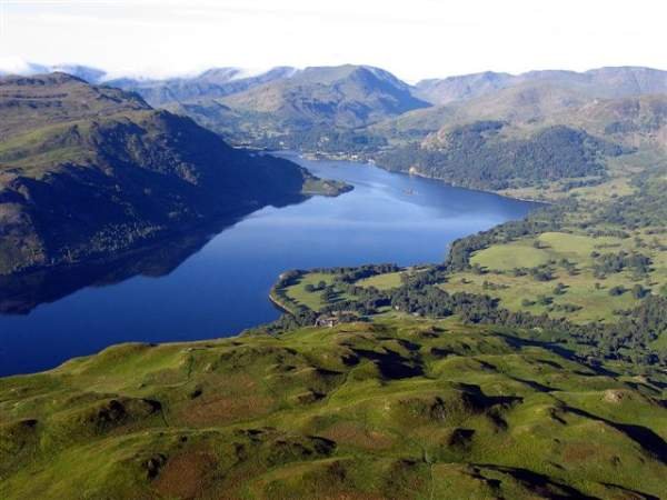 Aerial view of a deep blue lake winding through green hills and a valley with distant mountain ranges on the horizon. - Manchester Airport Taxi Transfer - Manchester Airport Taxi Transfer