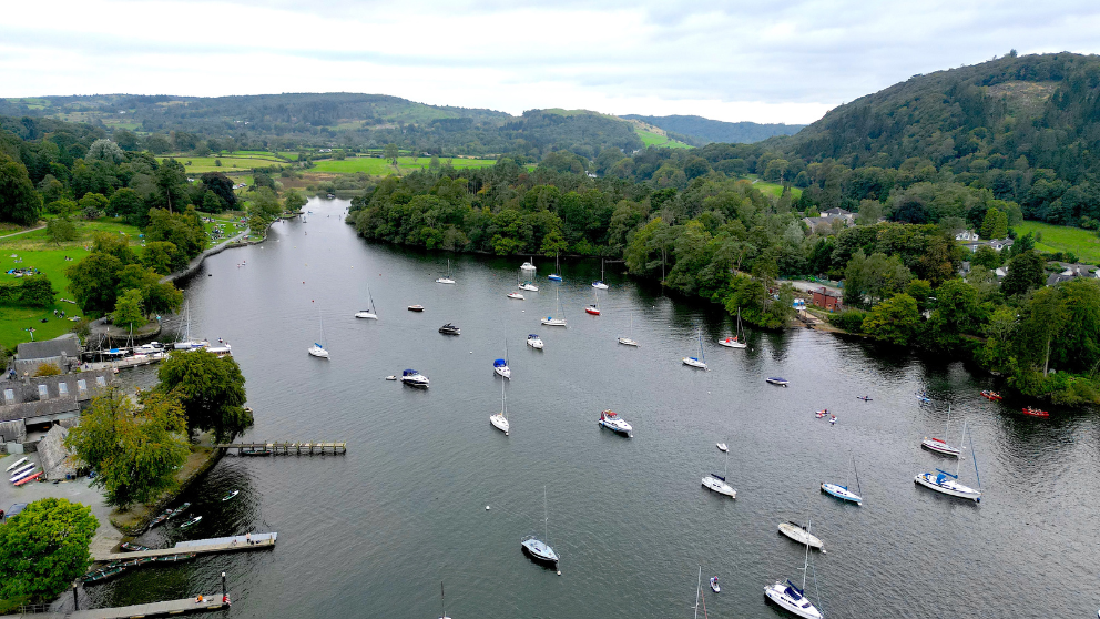A river winding through green countryside with numerous anchored sailboats and a village shoreline on the left under an overcast sky. - Manchester Airport Taxi Transfer - Manchester Airport Taxi Transfer